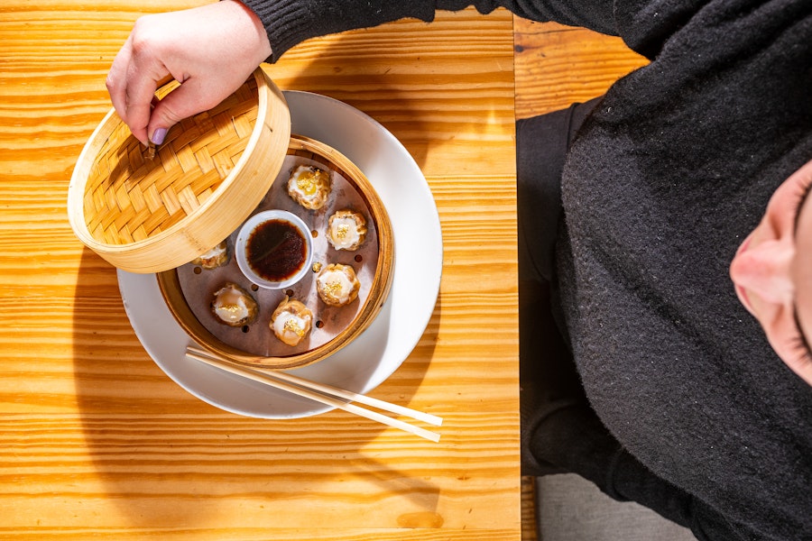 A diner lifts the lid of a bamboo steamer to reveal siu mai dumplings at China Chilcano.