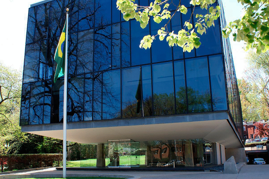 The modern, glass exterior of the Brazilian embassy with a flag out front. 