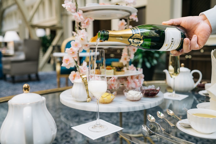 A hand pours champagne into a glass on a table set for a lavish high tea. 