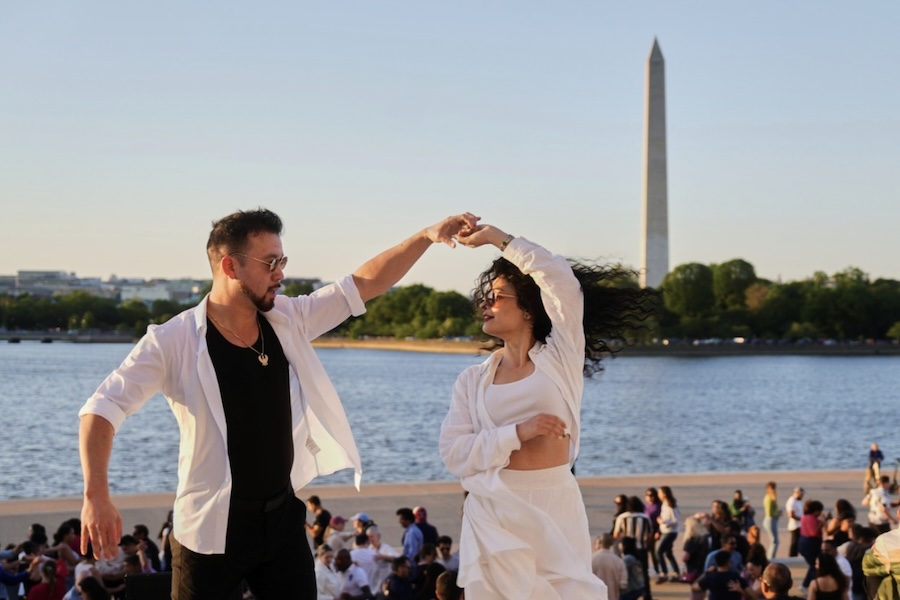 Two people dance with the Washington Monument in the background. 
