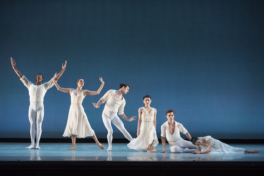 Six ballet dancers in white costumes perform a graceful contemporary piece on a minimal stage.