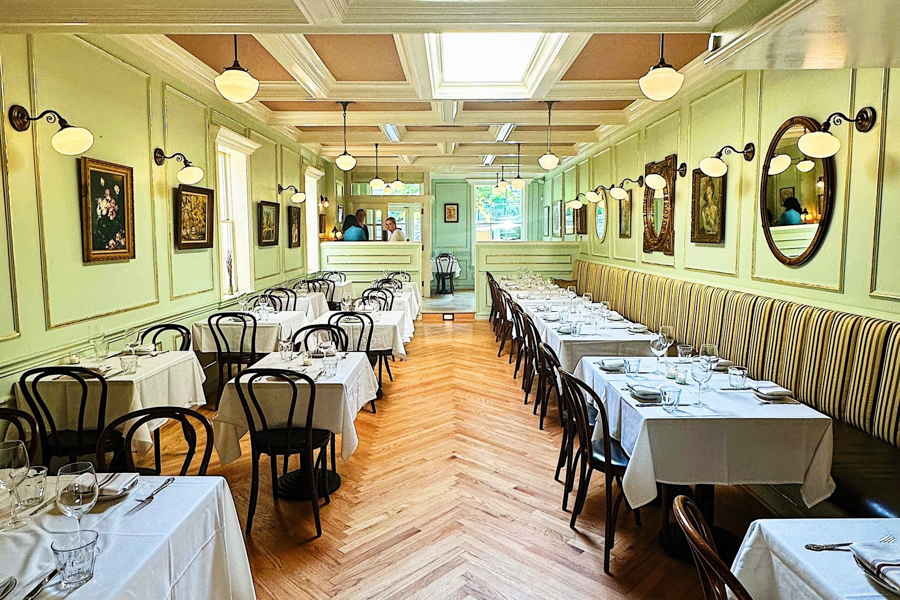 Elegant dining room at Chez Billy Sud in Washington, DC with pastel walls, wood floors, and white tablecloths.