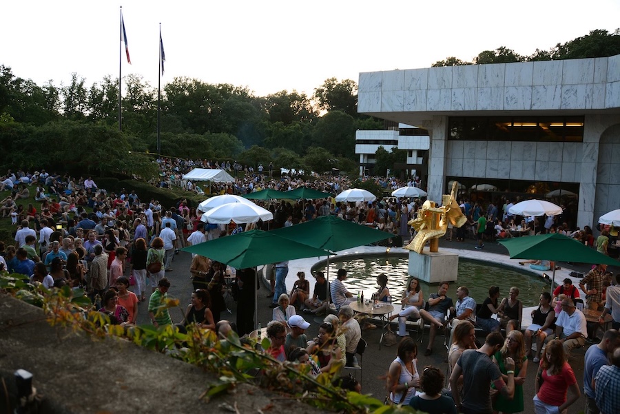 Crowds gather around the fountain and sculpture at the French Embassy in Washington, DC during a Bastille Day celebration.