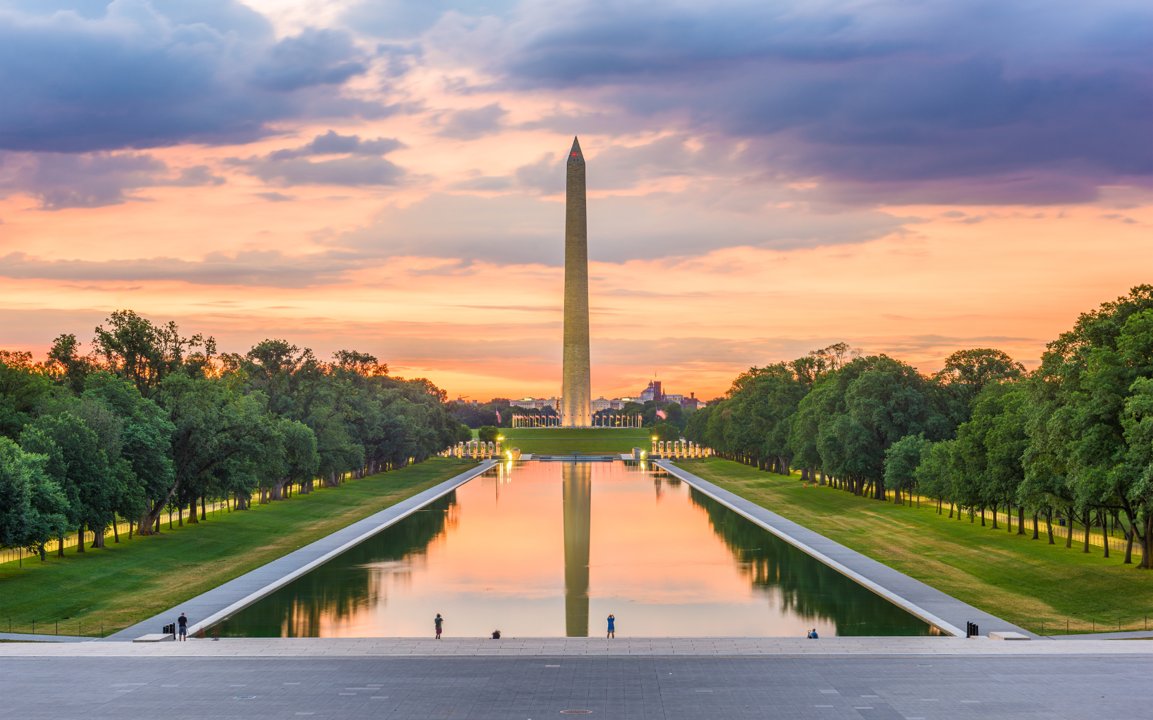 The Washington Monument glows at sunset with a colorful sky reflected in the Lincoln Memorial Reflecting Pool in Washington, DC.