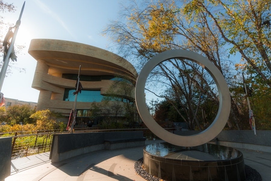 Circular sculpture in front of the National Museum of the American Indian surrounded by trees.