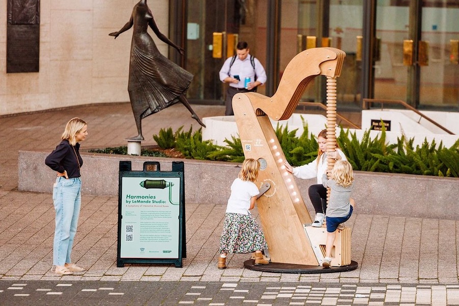 Children play with an art installation that resembles a large harp. 