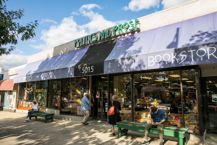 The entrance of Politics and Prose bookstore in Washington, DC, with people sitting on benches and browsing outside.