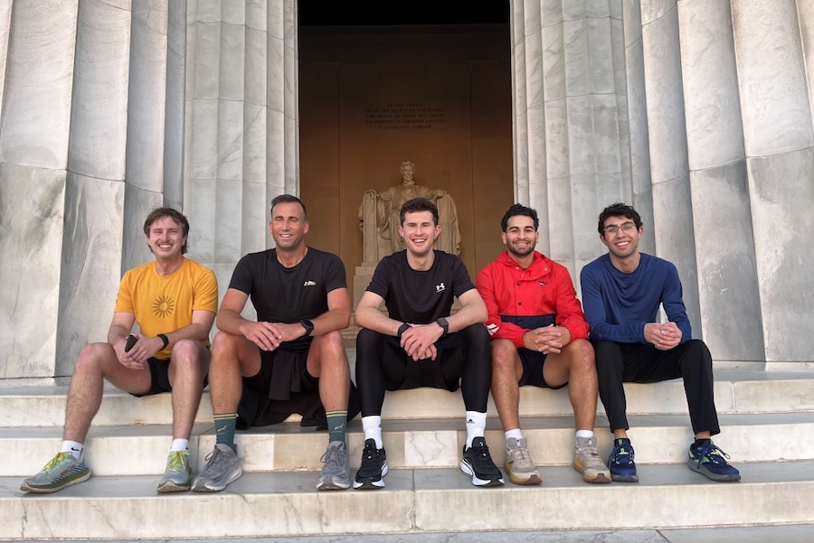 A group of runners sit on the steps of the Lincoln Memorial after a tour, with the statue of Abraham Lincoln visible in the background.