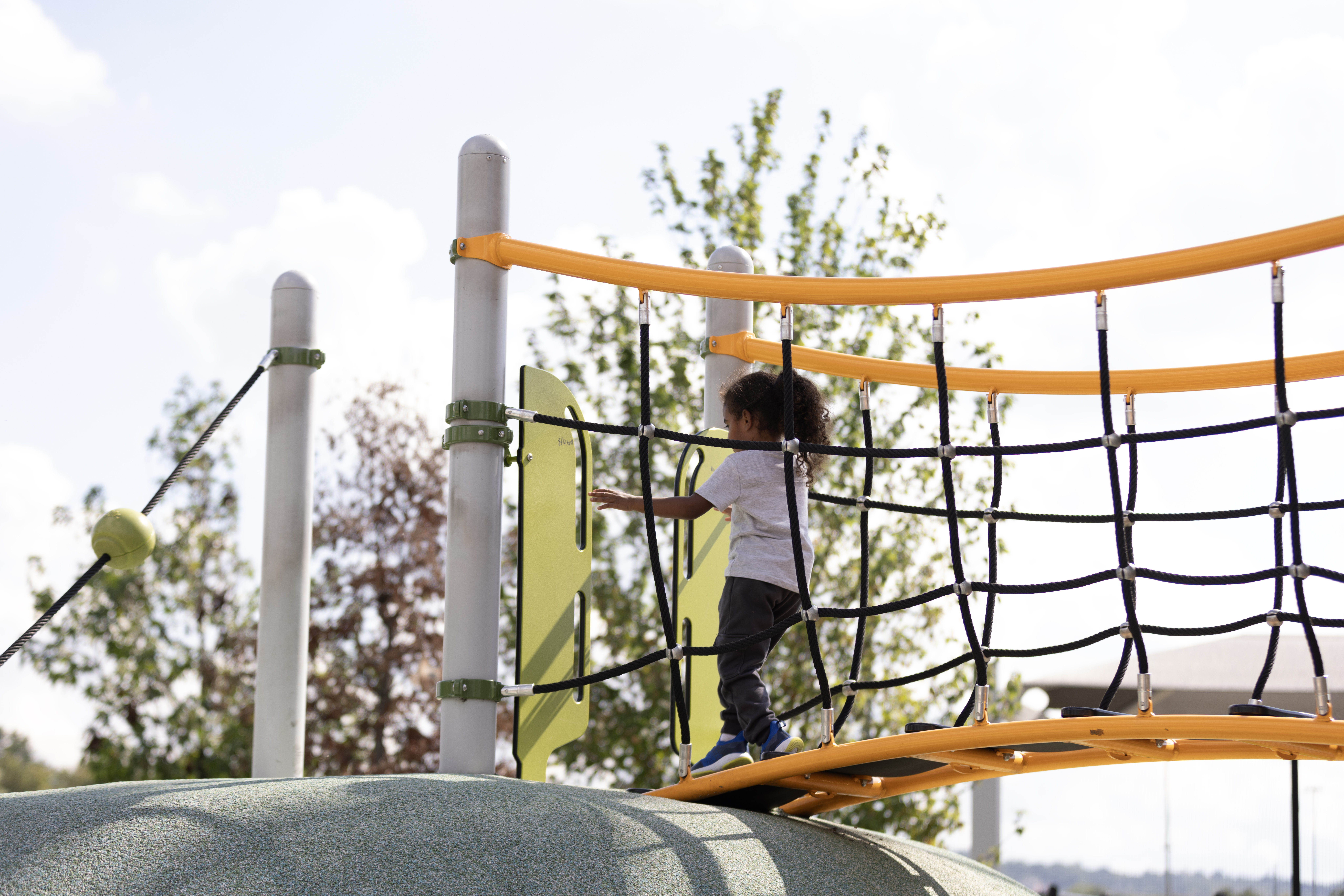 A young child climbs across a rope bridge on a colorful playground structure in Washington, DC.