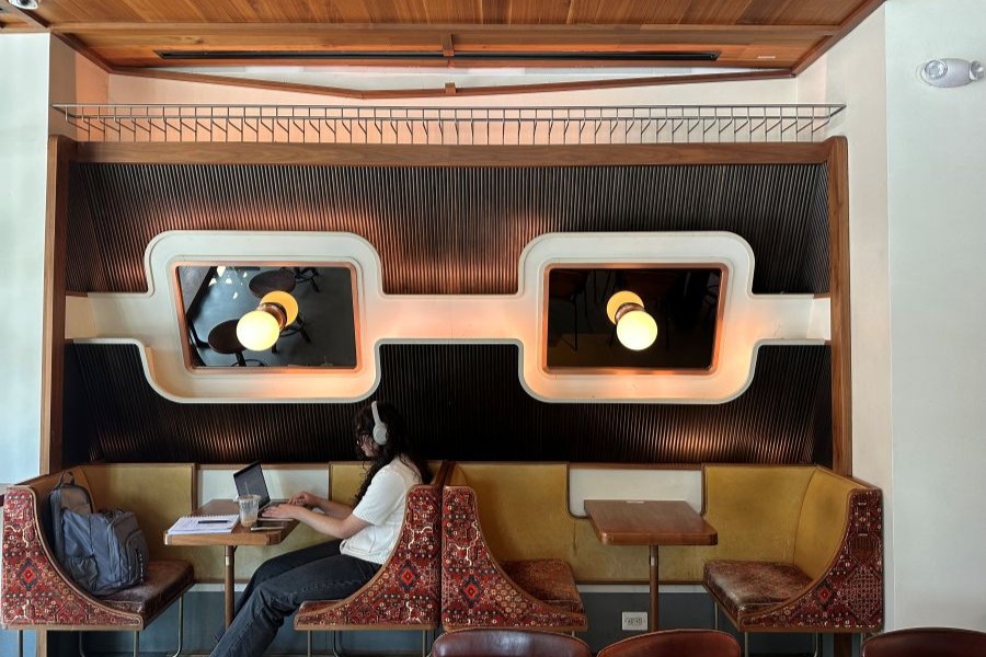 A person wearing headphones works at a booth in a stylish café with retro lighting and mid-century modern decor.