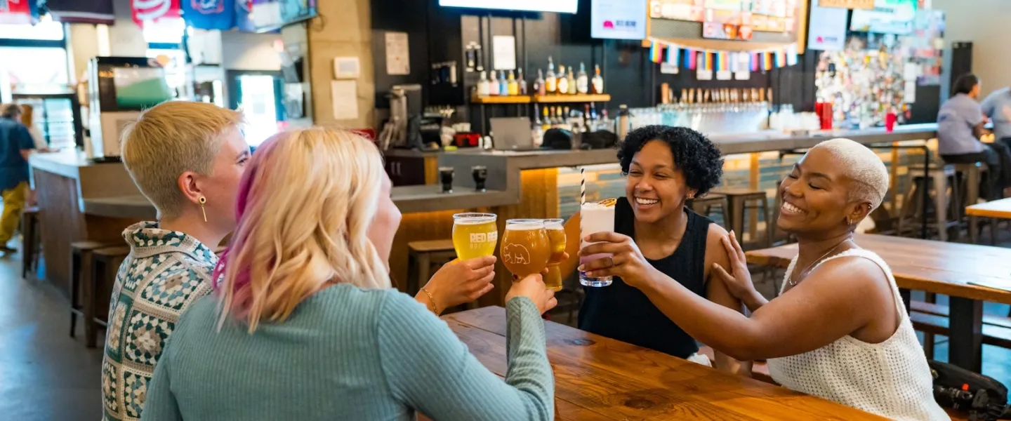 Four smiling people cheers in a cozy brewery. 