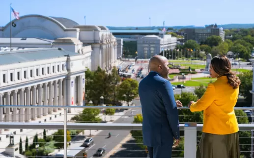 Two people looking out on Union Station with cars below 

