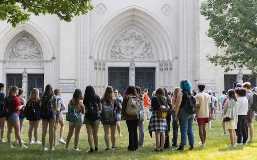 A group of people on a walking tour outside the Washington National Cathedral, standing on the lawn near the ornate stone entrance.