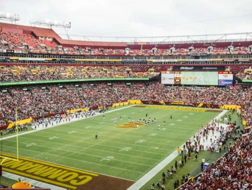 A packed stadium during a Washington Commanders football game, with fans filling the stands and players on the field at FedExField.