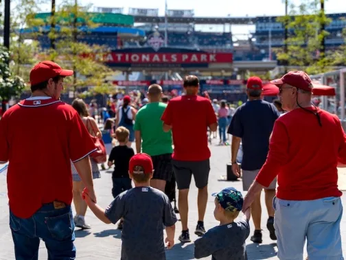 Families in red jerseys walking toward Nationals Park for a baseball game.