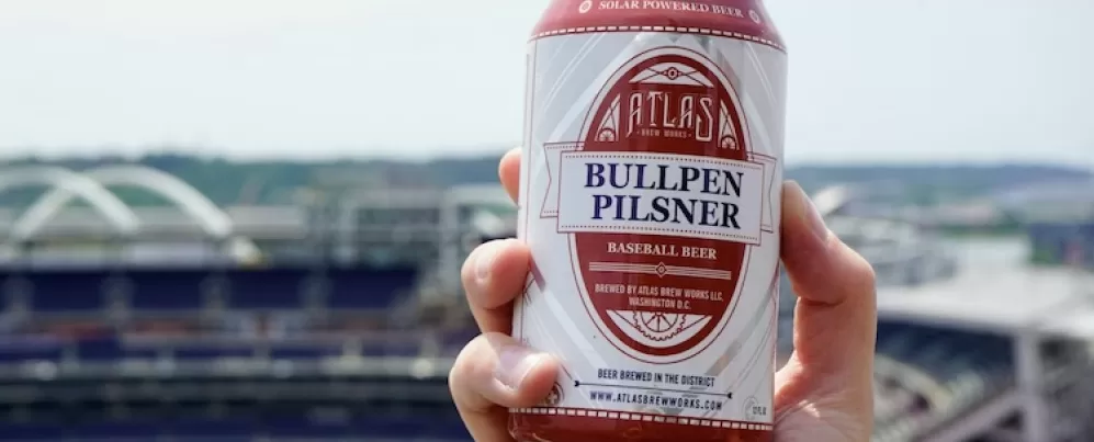 A hand holds a beer can with a view of Nationals Park in the background. 